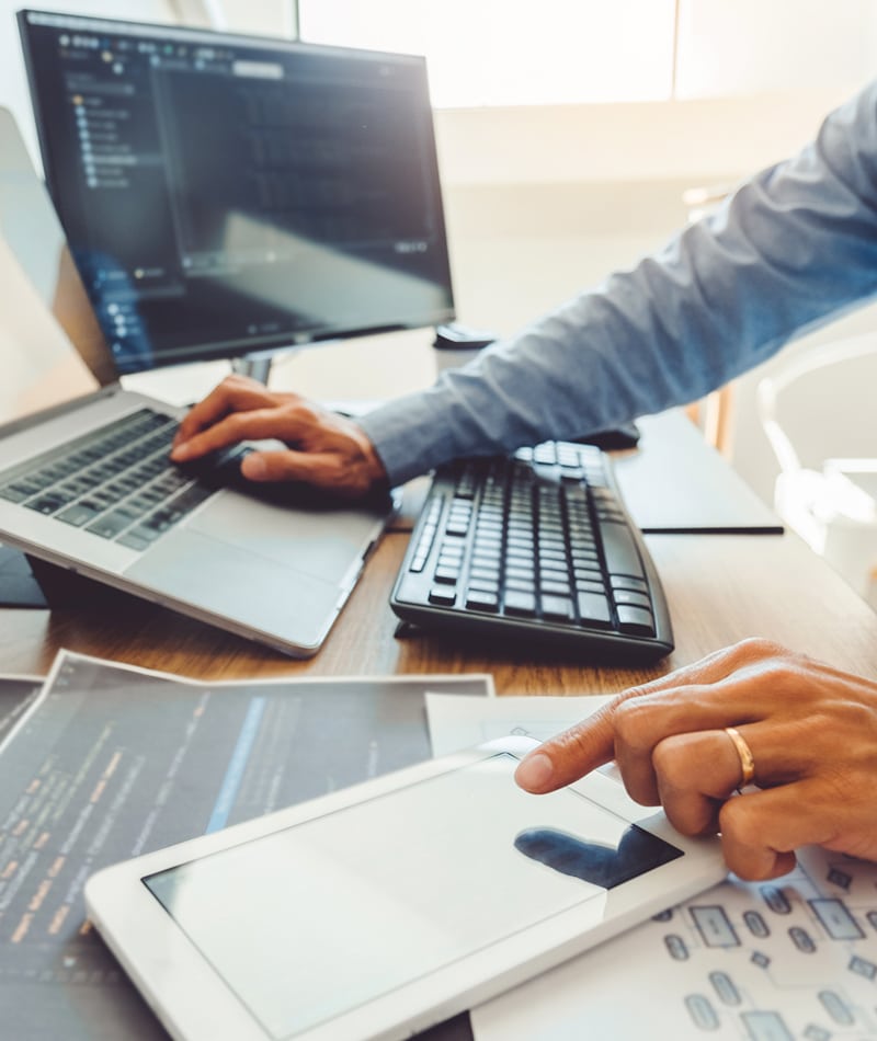 Close up of an IT support specialist managing a laptop, tablet, and monitoring systems.