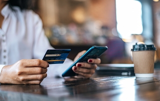 A woman holding a credit card while looking at her phone to complete an online transaction.