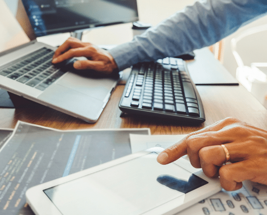 Close up of an IT support specialist managing a laptop, tablet, and monitoring systems for a Cypress business.